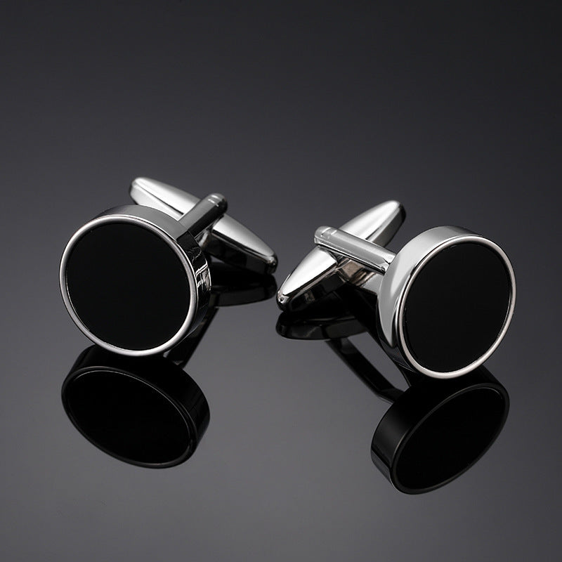A pair of silver-tone cufflinks with a round black enamel inlay and polished border on a dark surface