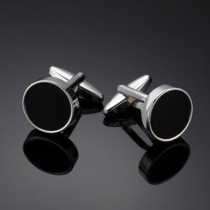 A pair of silver-tone cufflinks with a round black enamel inlay and polished border on a dark surface