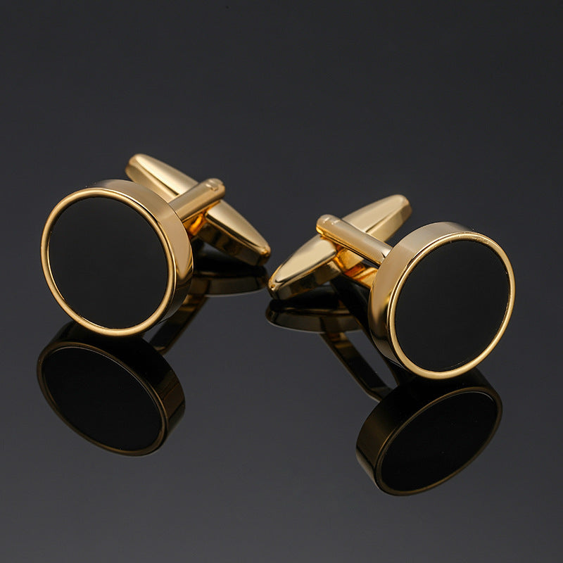 A pair of gold-tone cufflinks featuring a circular black enamel inlay and a polished metal border.
