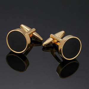 A pair of gold-tone cufflinks featuring a circular black enamel inlay and a polished metal border.