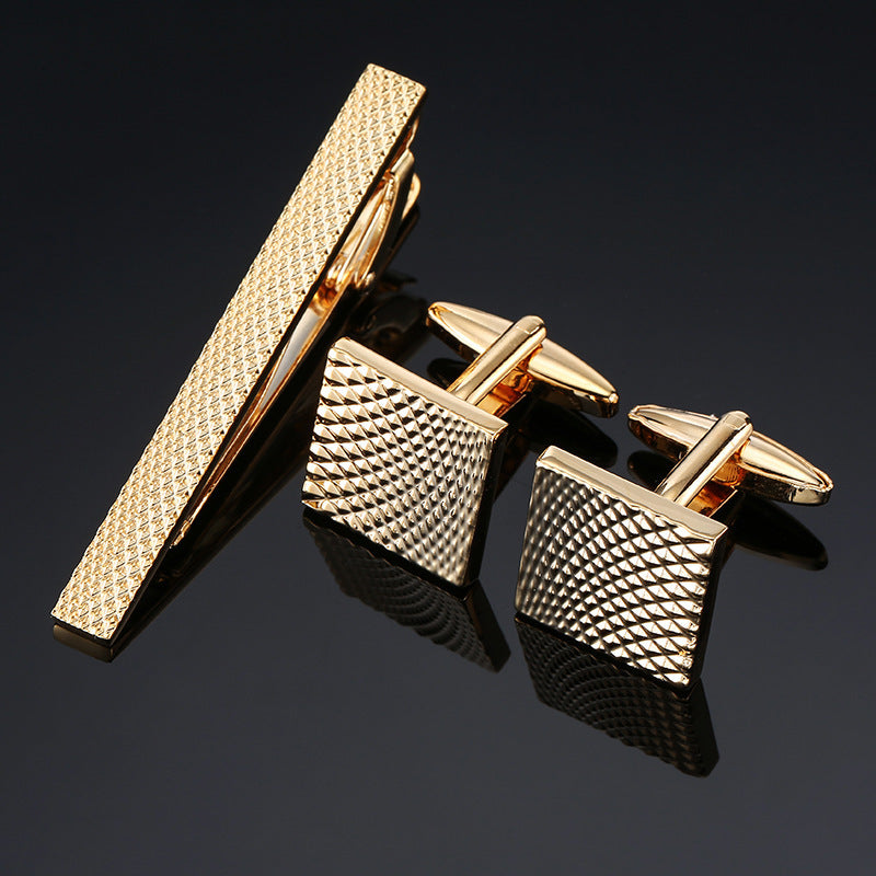A gold-tone tie clip and two square cufflinks with a pyramid-textured pattern.