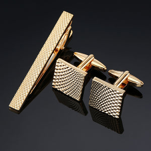 A gold-tone tie clip and two square cufflinks with a pyramid-textured pattern.