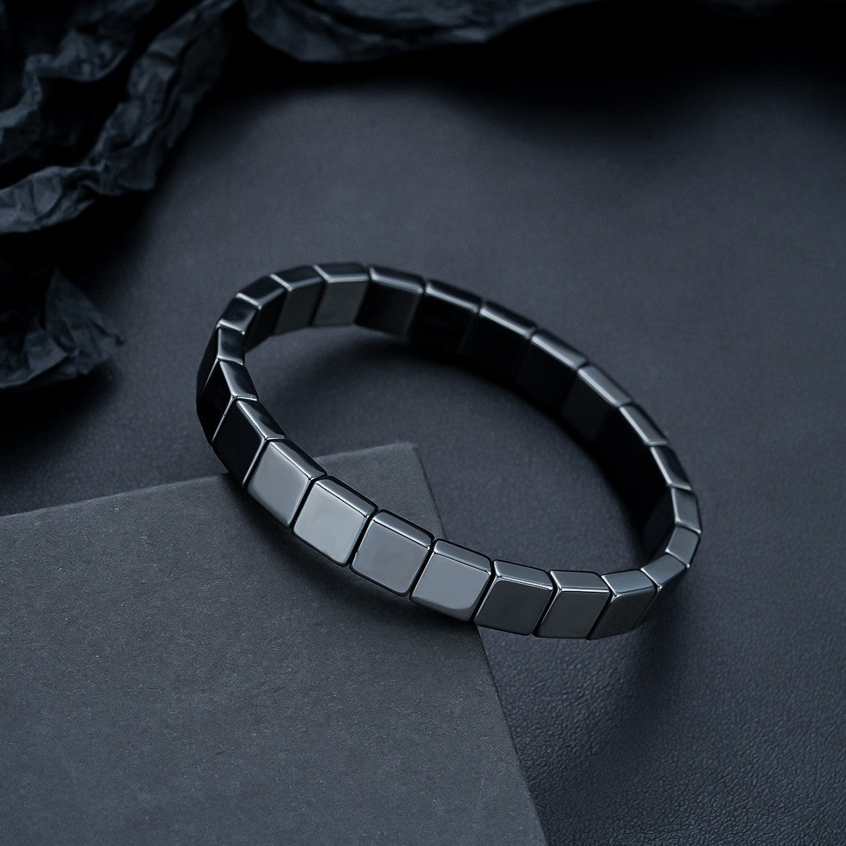 Men's dark metallic beveled square link bracelet on a flat surface